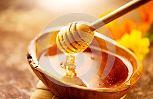 Honey dripping from honey dipper in wooden bowl. Healthy organic thick honey pouring from the wooden honey spoon