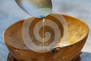 Honey dripping from a metal spoon into a wooden bowl