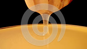 Honey dripping, pouring from a honey dipper on a black isolated background. Healthy organic thick honey dipping from a