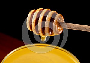 Honey dripping, pouring from honey dipper into glass bowl on black background. Healthy organic thick honey dipping from