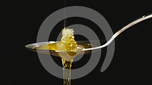 Honey dripping from the stainless tea spoon on black background