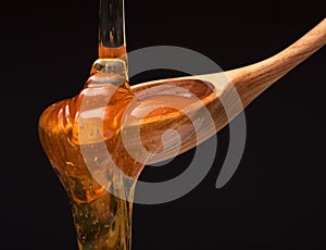 Honey dripping from a wooden honey dipper on black background