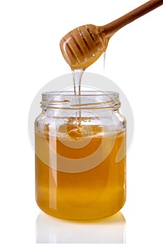 Honey dripping from wooden honey dipper in glass jar
