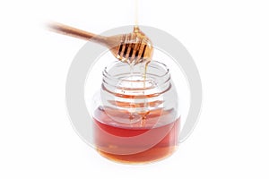 Honey dripping from a wooden honey dipper into the jar