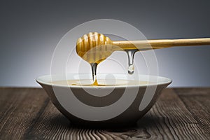 Honey drips from the spoon into a white bowl