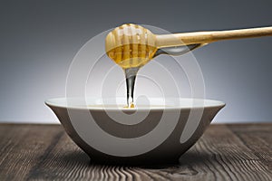 Honey drips from the spoon into a white bowl