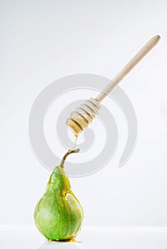 Honey drops from a honey spoon on a green pear in front of the white background, isolated