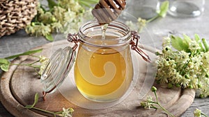 Honey flowing from a dipper into a glass jar, with fresh linden flowers in the background