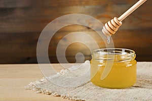 Honey flowing from honey dipper into the jar on wooden background