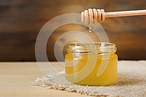 Honey flowing from honey dipper into the jar on wooden background