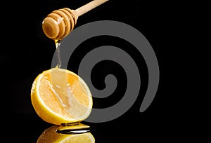 Honey flows down from a spoon to a lemon lying on a black background with copy space