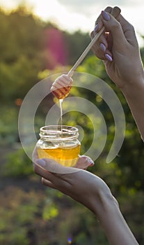 Honey flows from a special honey spoon into a jar against the background of the sunset and the garden
