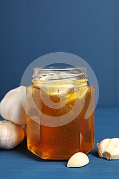 Honey with garlic in glass jar on blue wooden table