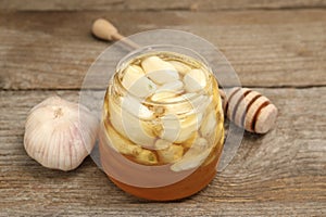 Honey with garlic in glass jar and dipper on wooden table, closeup