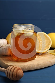 Honey with garlic in glass jar, lemons and dipper on blue wooden table