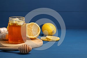 Honey with garlic in glass jar, lemons and dipper on blue wooden table. Space for text