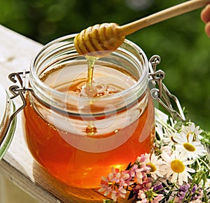 Honey in glass jar and flowers on a wooden floor