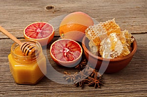 Honey in glass jar , honey combs in bowl with oranges and spices on wooden background