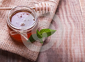 Honey in a glass jar, honey spoon and mint leaves on the wooden