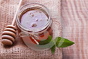 Honey in a glass jar,spoon and mint leaves on the wooden