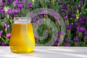 Honey in glass jar on wooden table on nature lavender background. Outdoor