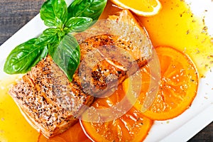 Honey Glazed fillet salmon with orange slices, spices and basil on white plate on dark background.