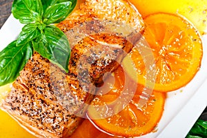 Honey Glazed fillet salmon with orange slices, spices and basil on white plate on dark background.