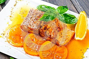 Honey Glazed fillet salmon with orange slices, spices and basil on white plate on dark background.