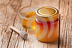 Honey in a jar and in a bowl, a wooden dipper on a wooden background, close-up
