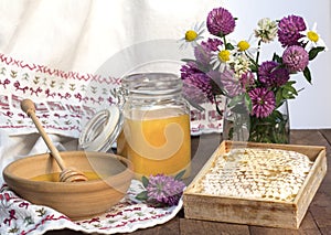 Honey in a jar and in a Cup and honeycomb with a honey spoon and on a background of white cloth and a bouquet of wild flowers