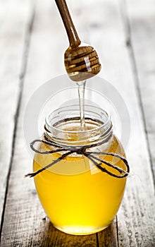 Honey jar with dipper and flowing honey on a wooden background