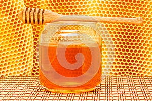 Honey in jar with dipper and honeycomb on mat