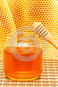 Honey in jar with dipper and honeycomb on mat