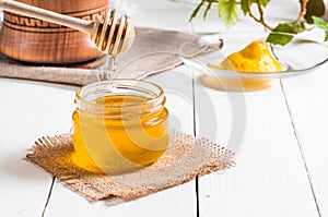 Honey jar with dipper and lemon flowing, wood background