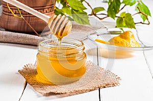 Honey jar with dipper and lemon flowing, wood background