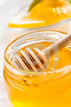 Honey jar with dipper and lemon flowing, wood background