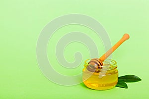 Honey in jar with leaves and honey dipper on colored background top view with copy text