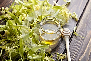 Honey in jar with linden flowers and honey dipper on wooden background