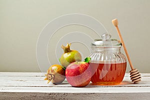 Honey jar, red apples and pomegranate on white wooden board