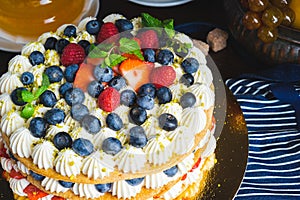 Honey layer cake with whipped cream, strawberries and blueberries on the table.