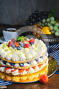 Honey layer cake with whipped cream, strawberries and blueberries on the table.