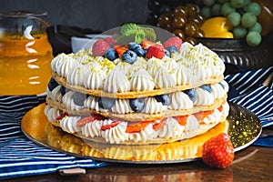 Honey layer cake with whipped cream, strawberries and blueberries on the table.