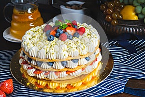 Honey layer cake with whipped cream, strawberries and blueberries on the table.