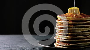 Honey or maple syrup is poured over a stack of pancakes with butter moving on dark background. High quality 4k footage