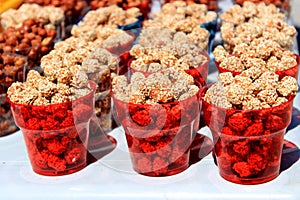 Caramelised eanuts with sesame seeds in red transparent cups.