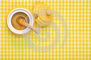 Honey pot and dipper on yellow background with copy space.