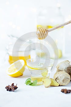 Honey is poured into a ginger drink in a cup. Ginger root, honey in a jar, lemon on a white table
