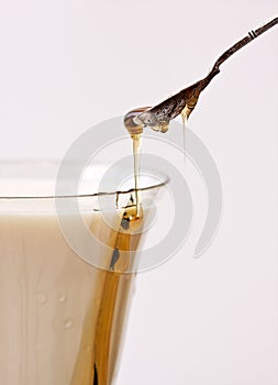 Honey poured into milk with spoon