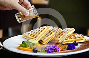 Honey pouring on a fresh waffles on a plate. Breakfast with waffles in morning