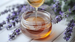 Honey pouring into a jar with lavender flowers on a white wooden background